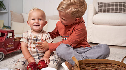 Two young boys happily playing with apples on the floor