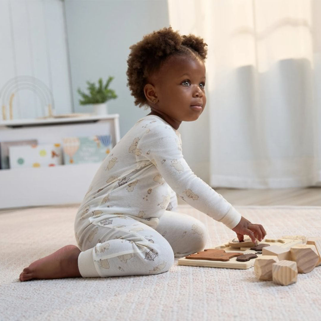 Little one in cozy cream-colored sleepwear with cute animal prints, playing with wooden toys on a light, airy rug. Snuggle up for less—grab adorable sleepwear during the $5 Frenzy Sale!