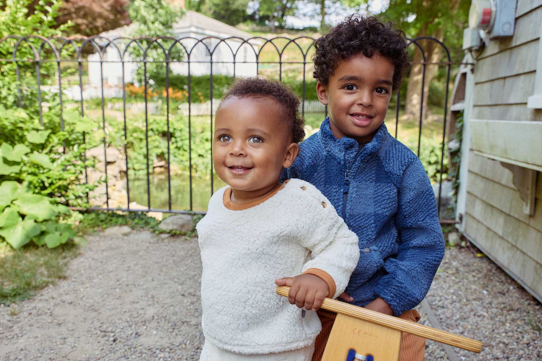 Two young boys joyfully hold a wooden toy in front of their house, showcasing their playful spirit and friendship