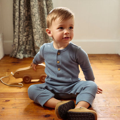  A toddler in blue pajamas sits on the floor, surrounded by toys, with a joyful expression on their face