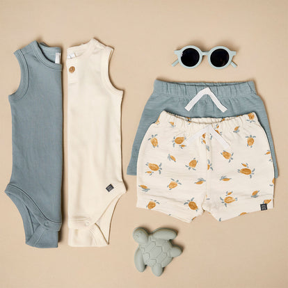  A curated flat lay of Gerber Childrenswear® modern moments™ neutral sleeveless tops, lemon-print shorts, and accessories, ideal for stylish spring mix-and-match outfits.